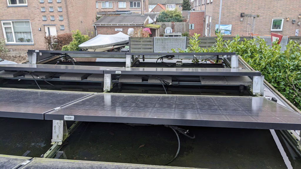 Foto van foutieve ballast, ongeschikte onderconstructie, losliggende kabels en foutief uitgelijnde onderconstructie. Door het gewicht is er wateraccumulatie waardoor het dak dreigt te bezwijken.