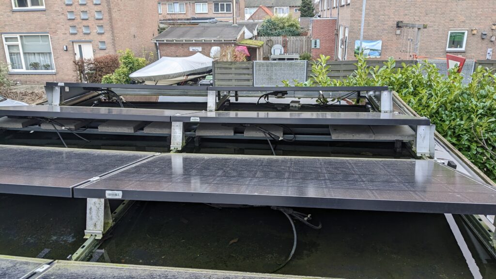 Foto van foutieve ballast, ongeschikte onderconstructie, losliggende kabels en foutief uitgelijnde onderconstructie. Door het gewicht is er wateraccumulatie waardoor het dak dreigt te bezwijken.