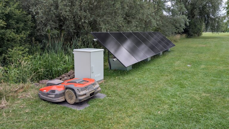 Overzichtsfoto van de hele opstelling. Links de robotmaaier, daarnaast de kast met omvormers en batterijen en rechts 8 PV panelen op de GSE onderconstructie.